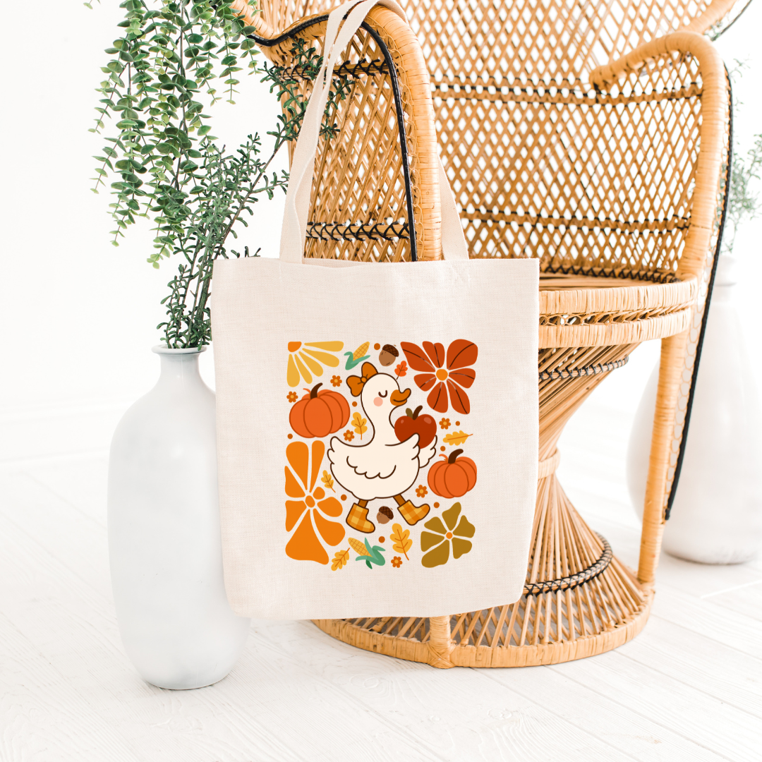 Tote bag with a chicken and pumpkins design on a wicker chair with a plant in the background