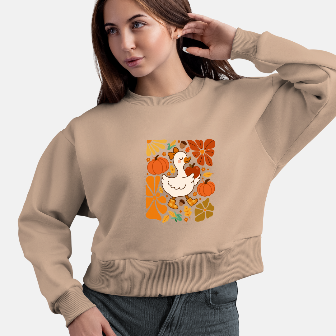 Woman wearing a beige sweatshirt with a graphic design of a duck, pumpkin, and autumn leaves.
