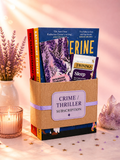 Book subscription box labeled 'Crime/Thriller Subscription' with books inside, on a decorative surface with flowers and candles.